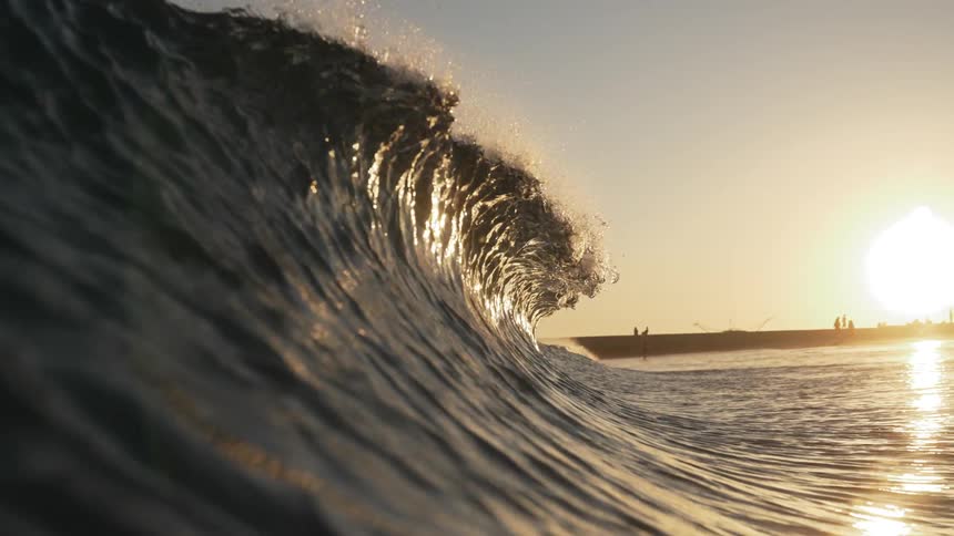 A small ocean wave breaks on a beach at sunset