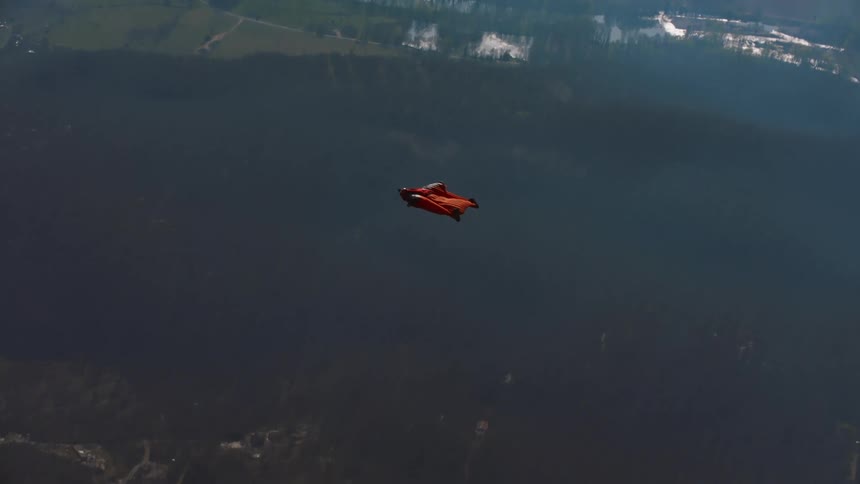 A person hang glides through the sky far above a neighborhood below