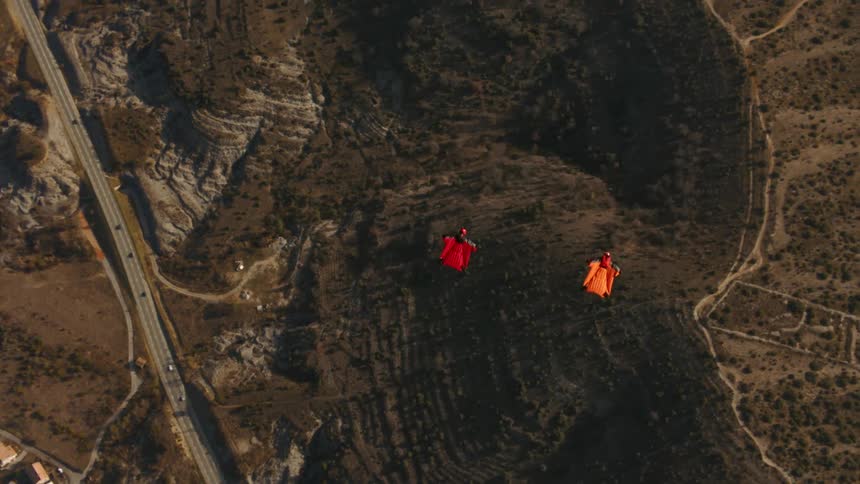 People fly with wingsuits over town in scrubland