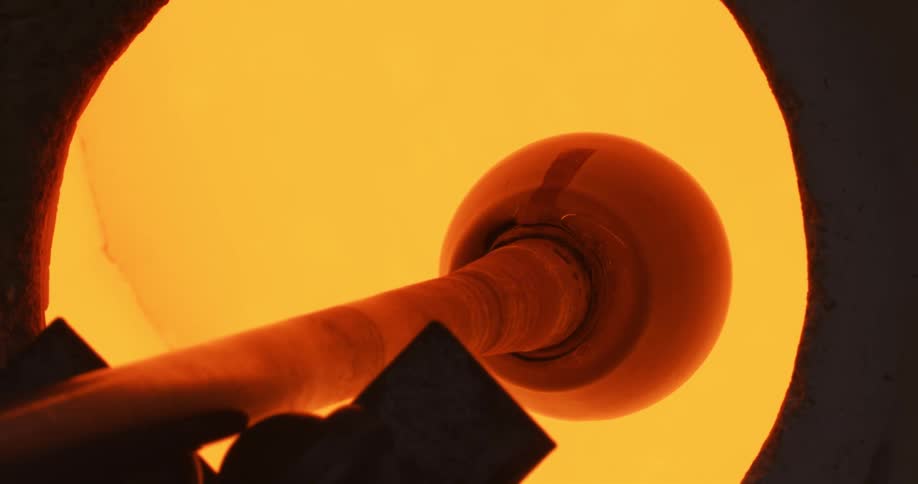 Molten glass at the tip of a pipe turning inside a hot oven