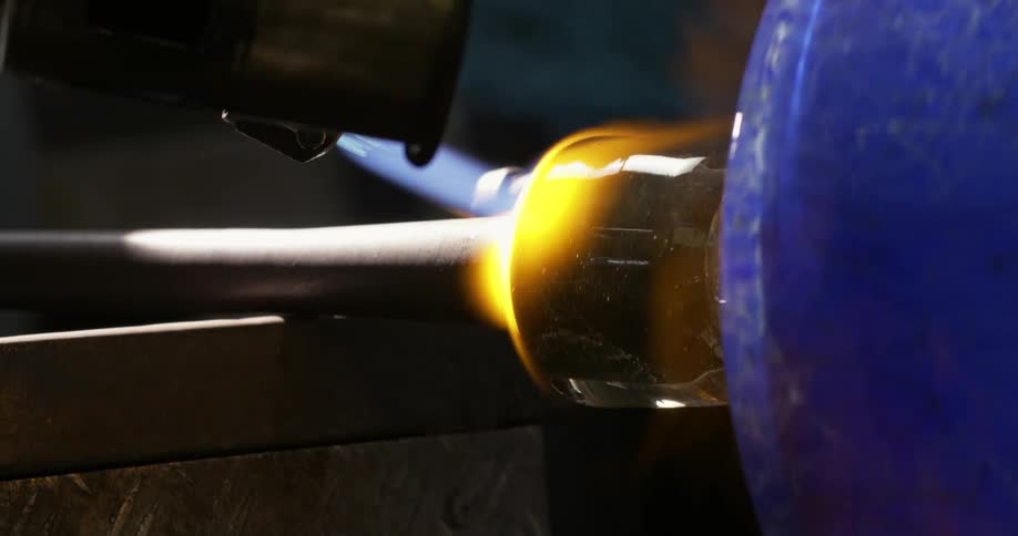 A glass vase being melted by a blowtorch while it is being rotated