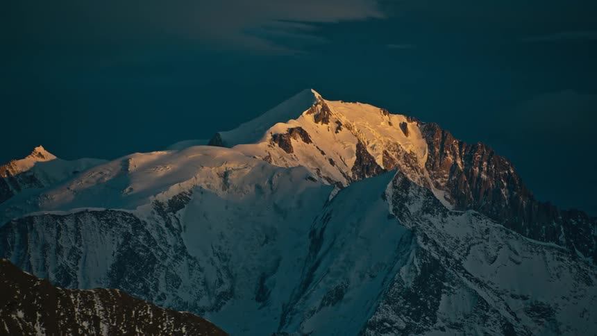Sunlight shines on a snow covered mountain ridge under a dark sky