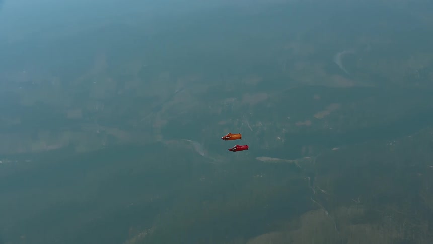 Two skydivers wearing wingsuits are floating over the land below as they slowly descend