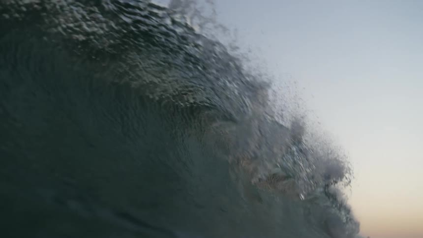 A large ocean wave forming a white crest and crashing with crystal clear water at sunset