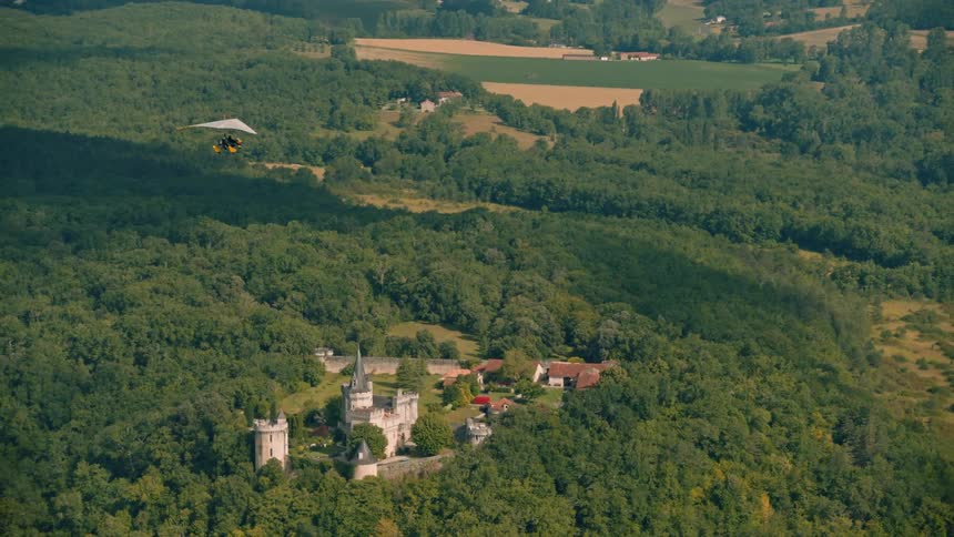 Aerial view of a powered glider flying over a castle in the countryside