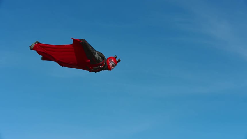 A skydiver wearing a wingsuit flies across the blue sky and looks down