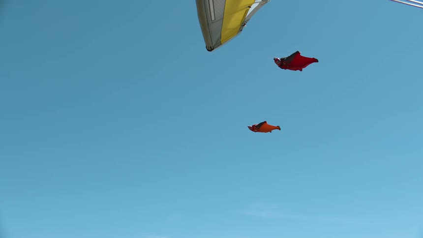 Two people wearing red wingsuit are gliding in the sky