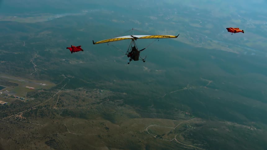 One person flying in a hang glider and two next to them flying in flight suits