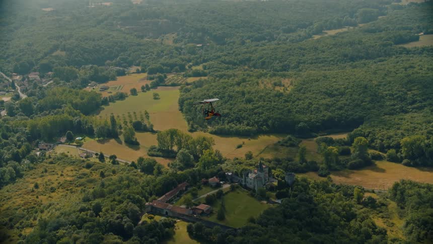A parachute floats in the air about a large area of land full of trees