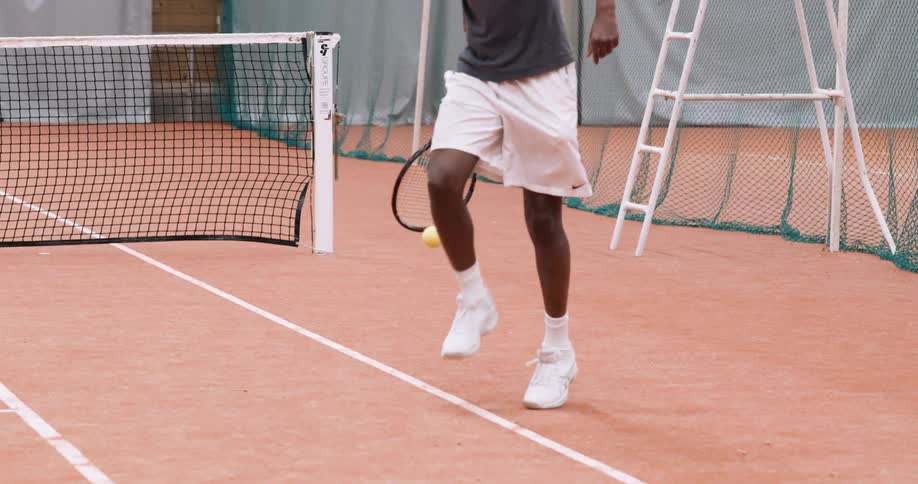A man picking up the tennis ball with his racket and the support of his foot on a tennis court