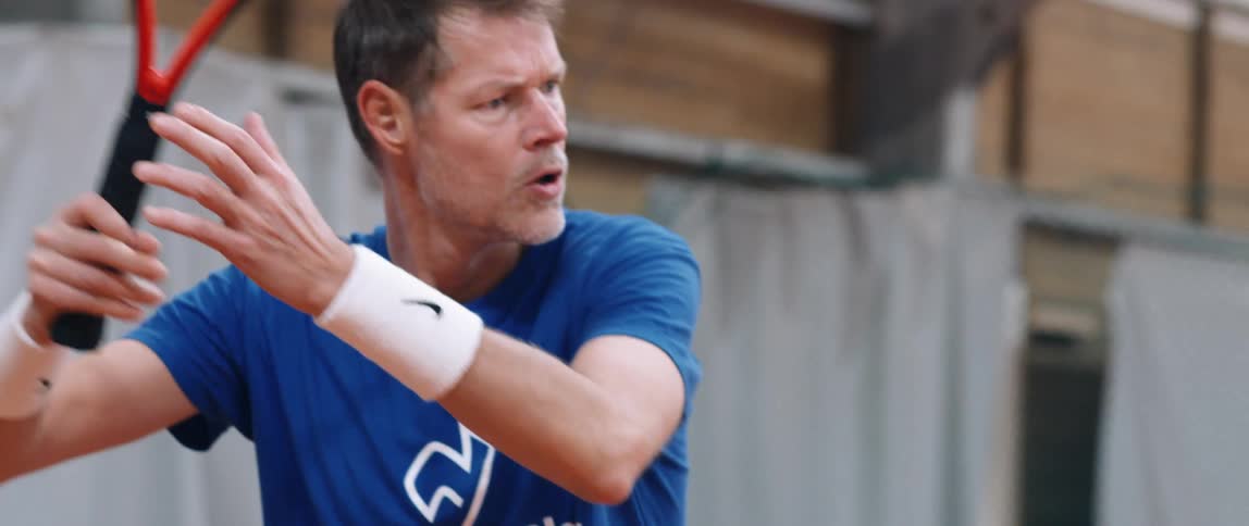 A man playing tennis hits the ball with the racket at midday