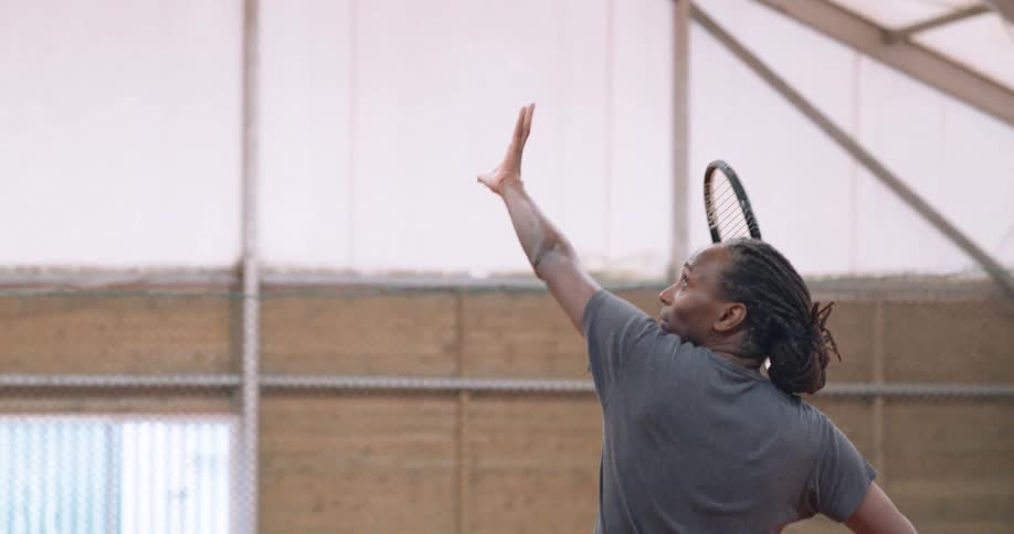 A man playing tennis and throwing a ball on an indoor and covered court