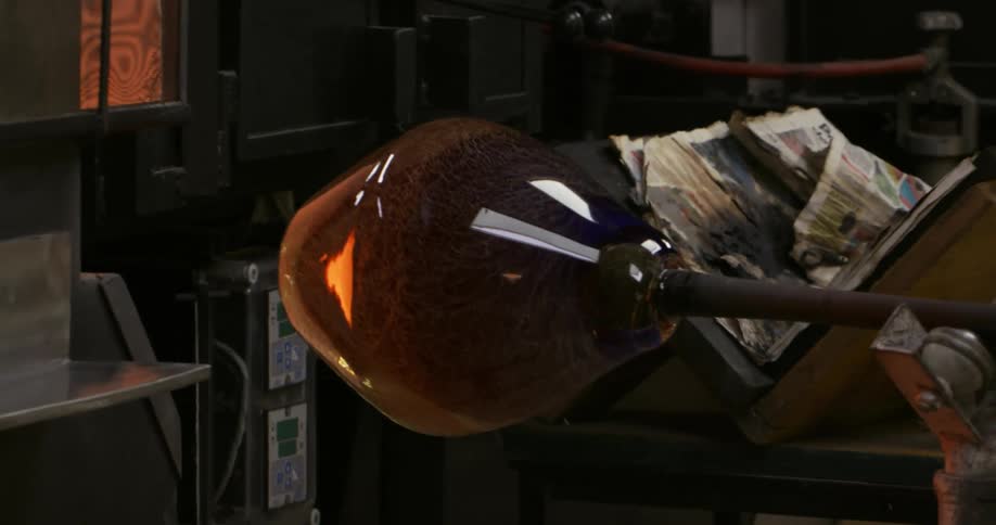 An iron rod holding a glass vase spinning and entering a forge