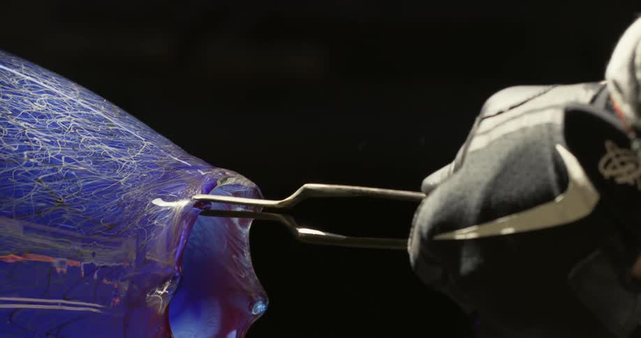 Artisan uses metal thongs to shape the mouth of a glass vase
