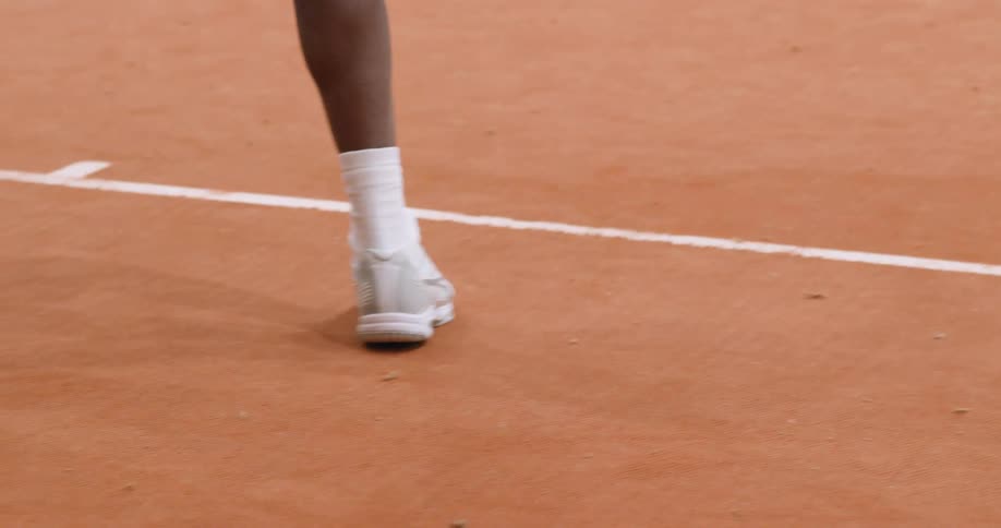 A tennis players feet are moving around across a clay court
