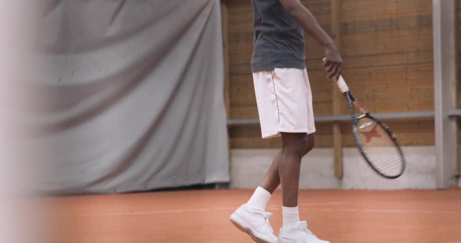 A tennis player on a laminate court grasping a racket and bouncing in anticipation