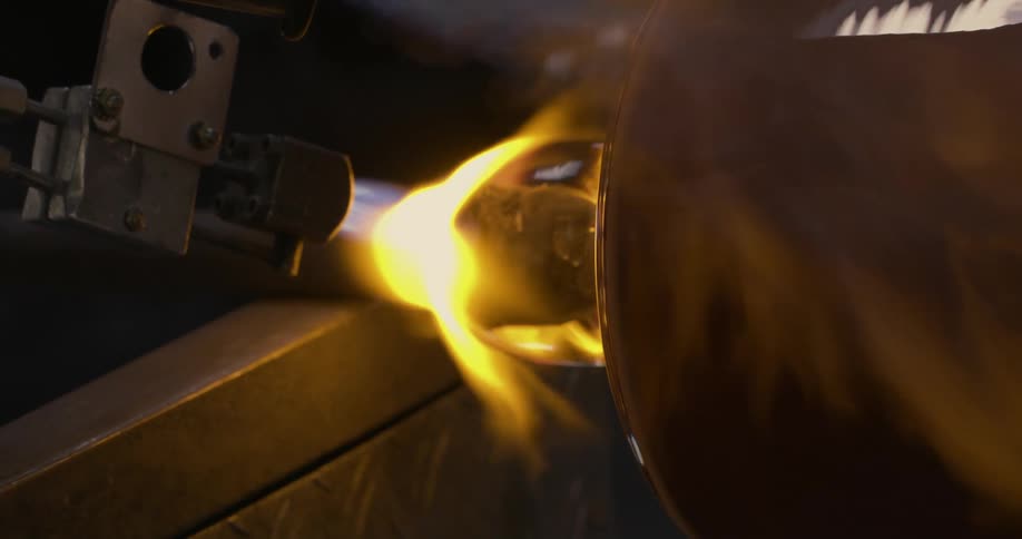 Torch heats base of glass attached to shaft while second torch heats glass cylinder