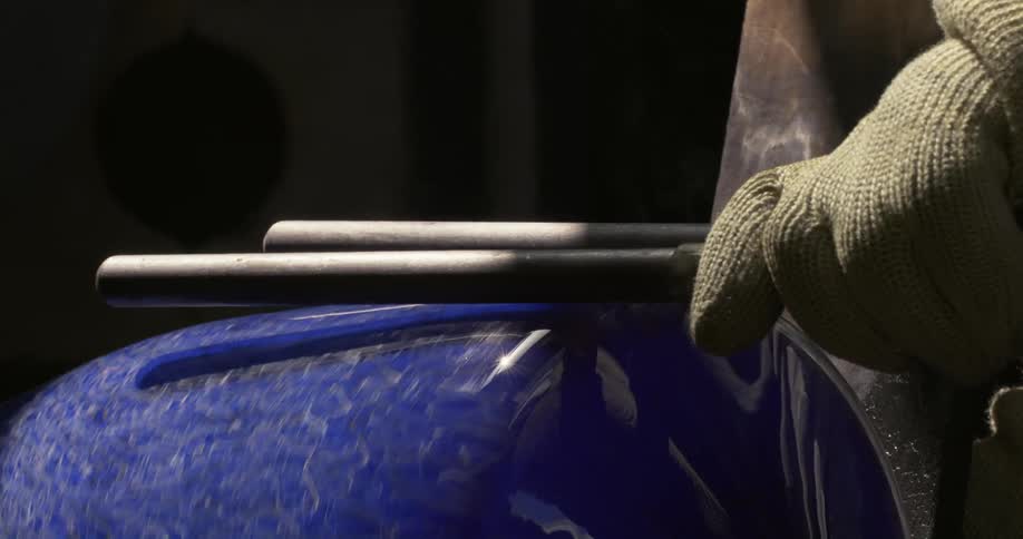 A person using a tool to shape a blue vase that is rotating