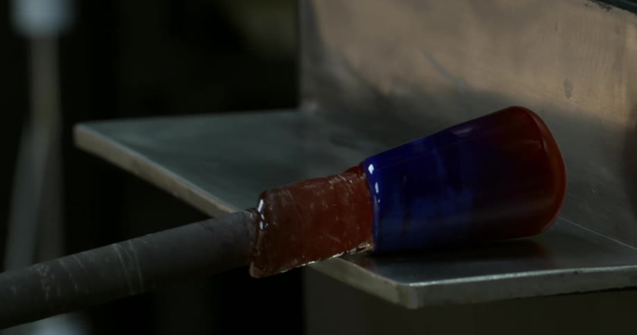 A piece of hot glassware takes shape over a metal surface