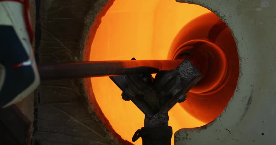 A persons hand rotating a steel inside a round opening with orange light from a flame