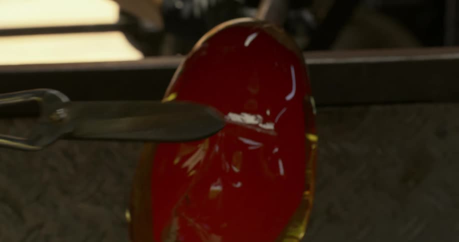 A human hand cutting a portion of the glass in its liquid state during the formation of a vase