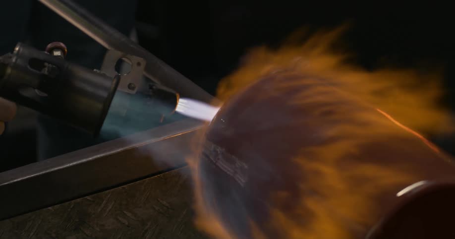 A person using the tools to intensely heat and fire the metal barrel in a workshop
