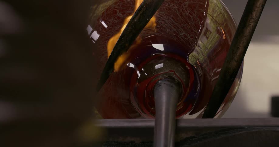 A piece of hot glassware spins under metal thongs shaping its neck