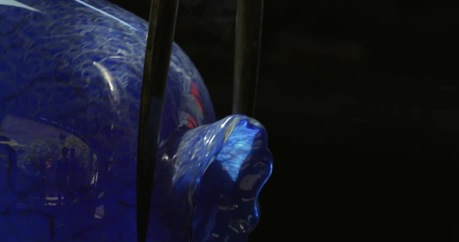 A person placing a sharp iron tool on top of a blue vase that is rotating