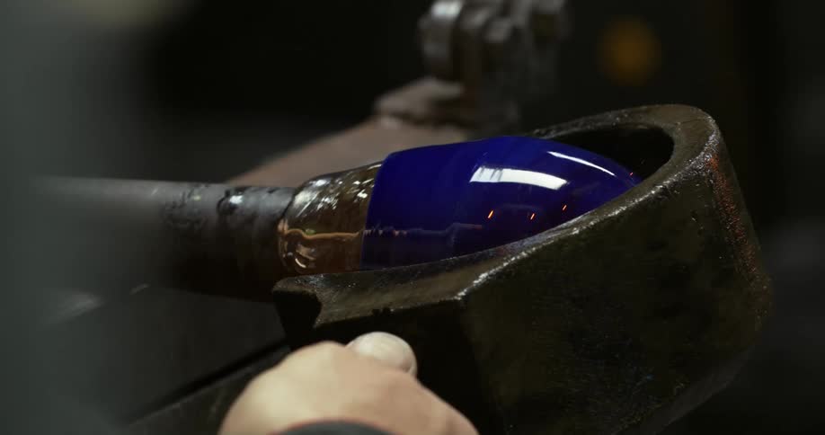 A person is shaping molten blue glass on a tube