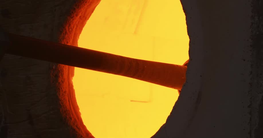 A glass vase being removed from a forge by a metal rod