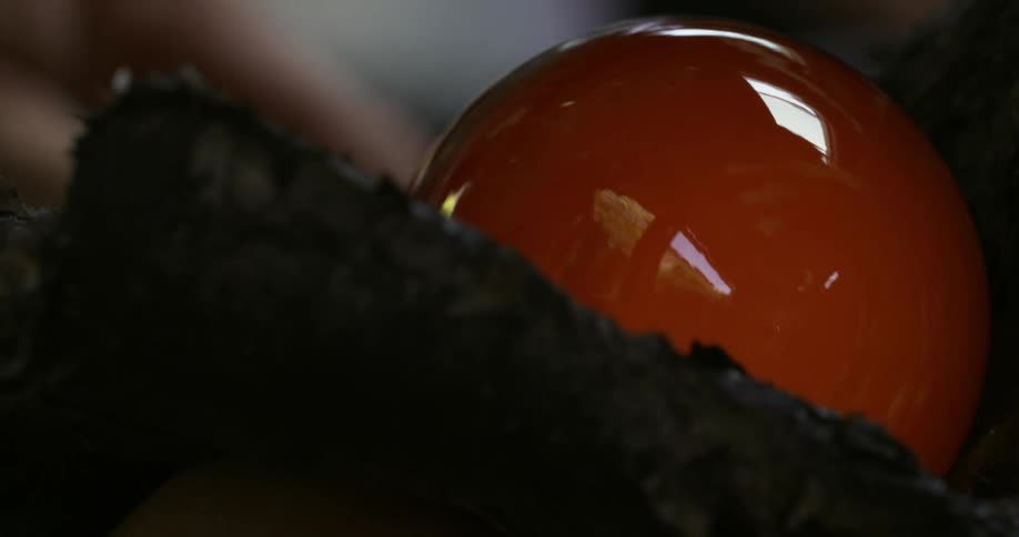 Glass maker rotates glass globe shaping it against roughsurface