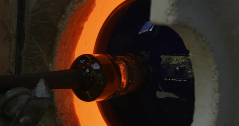 A large brown glass jug is being fashioned in a hot kiln furnace