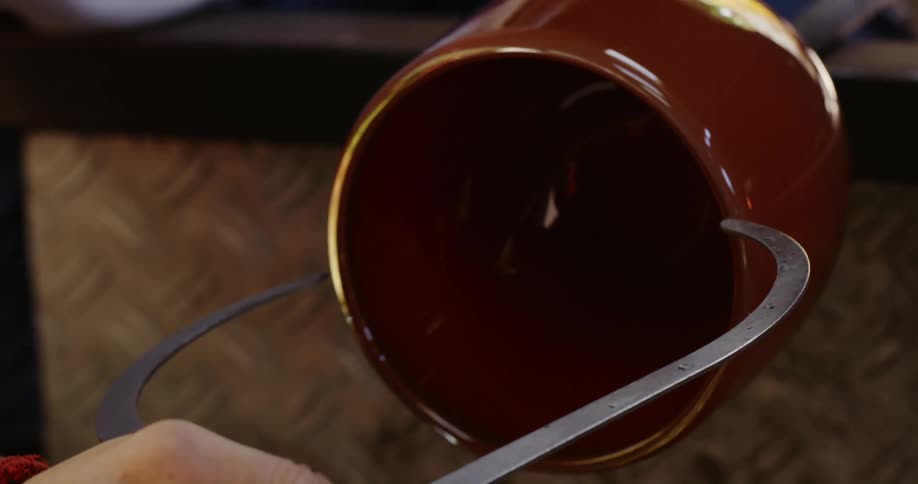 A person uses a metal tool to etch gold around the rim of a mug
