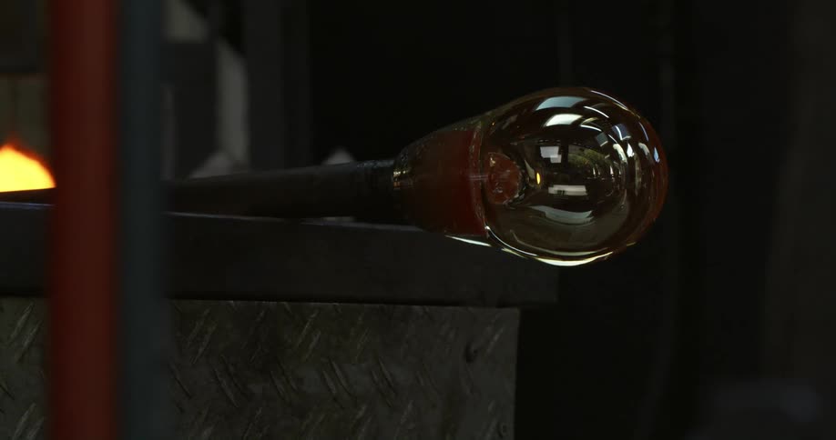 A tapered clear glass bulb on the end of a pole that is rolling along a wall ledge