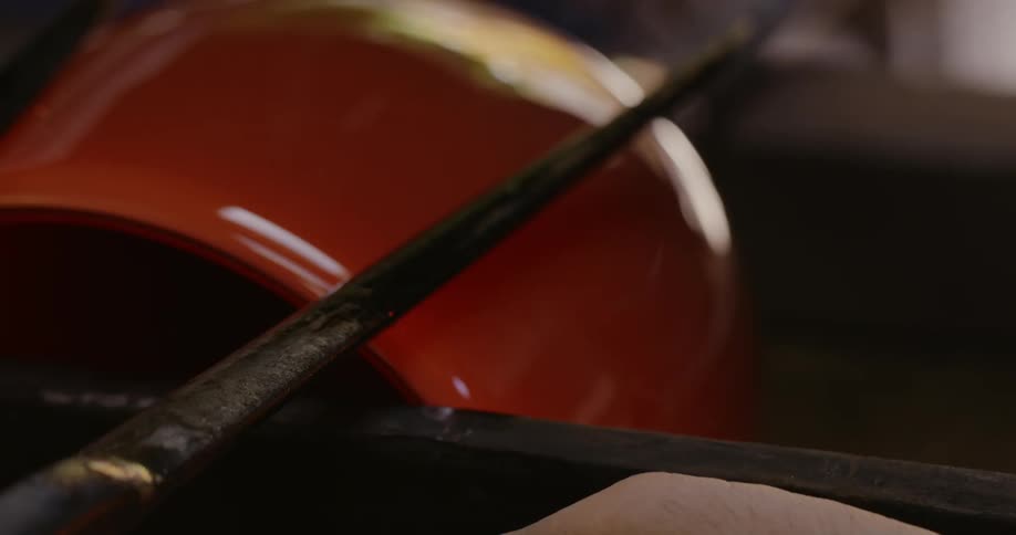 A red vase being shaped by an iron rod and the friction is making smoke