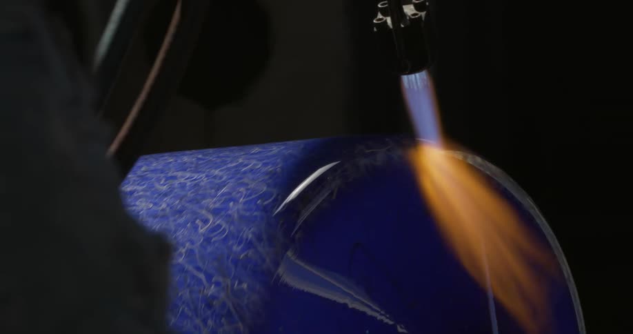 Glass maker uses torch on rotating glass cylinder