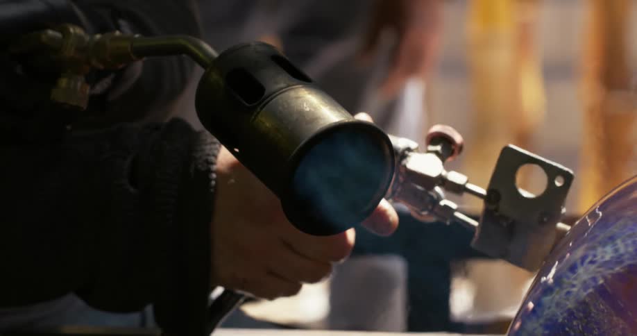 A person uses a metal tool to grind something they are making on a wheel