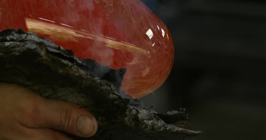 A persons hand holding something to mold melted glass
