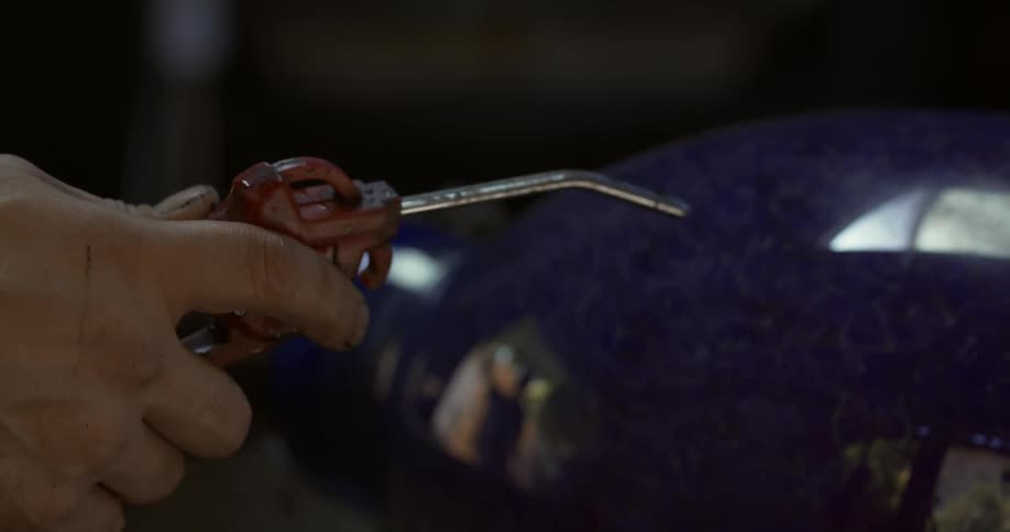 A person passing a tool through a glass vase that is rotating