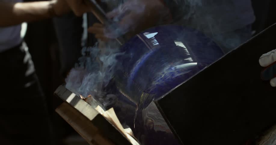 Two people are rotating a glass vase and heating it until smoke comes out