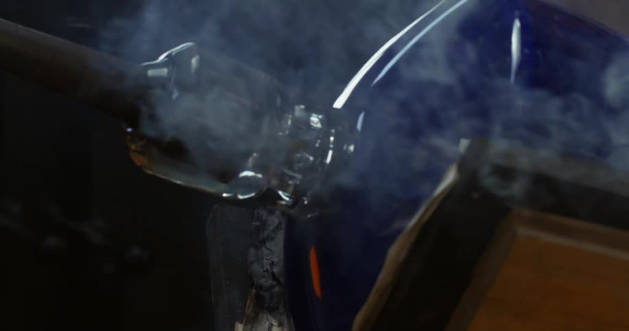 Smoke rises from furnace as glass cylinder is turned in heat
