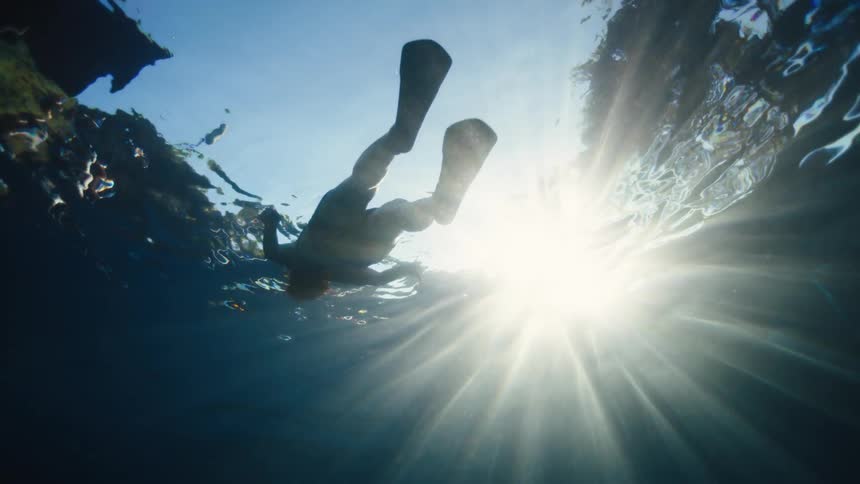 Underwater view of a person floating in the pool on a sunny day