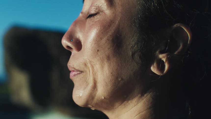 Woman sits beside a pool at sunset while meditating