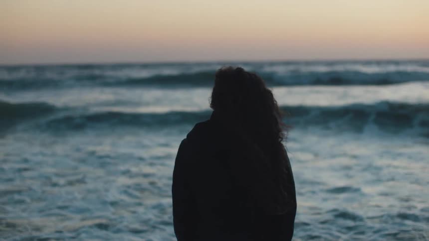 A silhouette of a person looking at the waves crashing on a beach