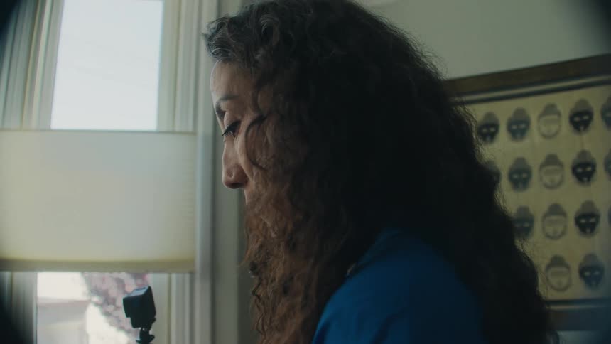 A woman is looking down doing a task with her hands by a window