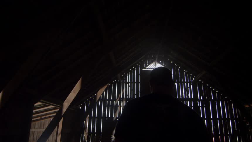 A man walks in a dark barn towards the door