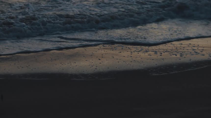 Closeup of the sea tide washing over a sandy beach at sunset