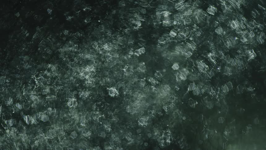 Ripples flow across surface of water as shapes move underneath