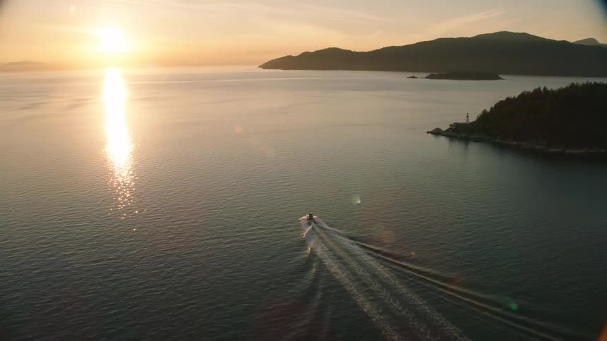 Two boats leave wakes while heading toward sun sitting just above the red horizon