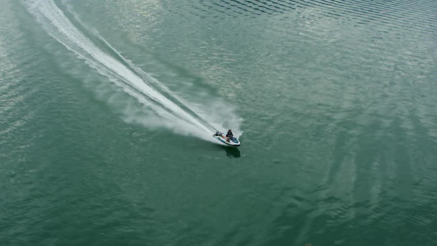 Woman rides jet ski past coast leaving a wake